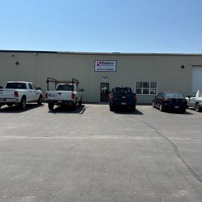 A Builders FirstSource facility in Idaho Falls, specialized in window and garage door installation services, with a parking lot in front featuring a white company truck and two other vehicles.