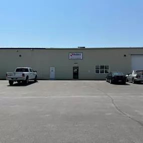 A Builders FirstSource facility in Idaho Falls, specialized in window and garage door installation services, with a parking lot in front featuring a white company truck and two other vehicles.