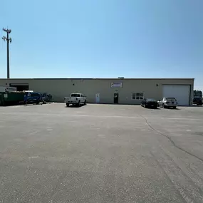 A Builders FirstSource facility in Idaho Falls, specialized in window and garage door installation services, with a parking lot in front featuring a white company truck and two other vehicles.