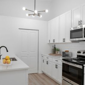 A kitchen with hardwood-style flooring, a modern chandelier, stainless steel appliances, a subway tile backsplash, a pantry, and a breakfast bar.