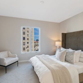 A bedroom with a large window and plush carpet flooring.