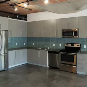 an empty kitchen with stainless steel appliances and gray cabinets at Binford Lofts in Los Angeles, CA 90013