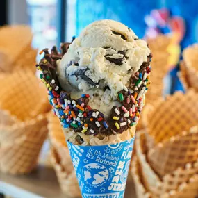 A Ben & Jerry's freshly baked dipped waffle cone with sprinkles in front of waffle cone display.