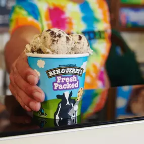 Scooper handing a fresh packed pint over the counter at a Ben & Jerry's ice cream shop.