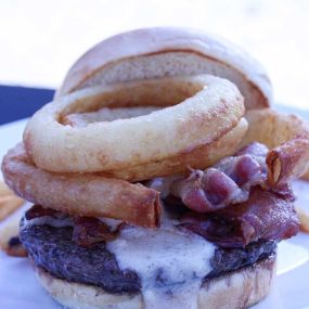 Cowboy Brew Burger.  1/3 Pound Grass-Fed Burger Topped with Crunchy Onion Rings, Rock Valley Brewing Brown Ale Beer Cheese, Bacon & BBQ Sauce on a Toasted Bun with French Fries.