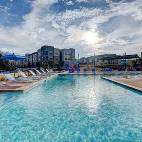 a large swimming pool with chaise lounge chairs and the sun shining over the water at The Jane at Preston Trail