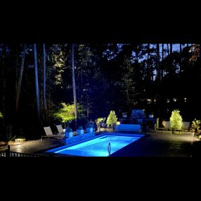 A pool, patio, and outdoor kitchen lit up at night.