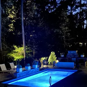 A pool, patio, and outdoor kitchen lit up at night.
