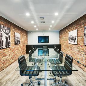 a conference room with a glass table and chairs and an exposed brick wall