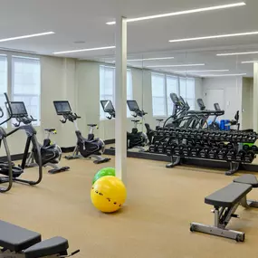 a gym with cardio machines and weights and a yellow ball on the floor