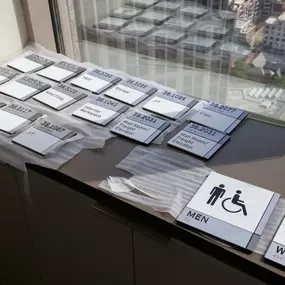 ADA signs on a desk featuring men's and women's wheelchair-accessible signage, designed by The Sign Factory Inc.