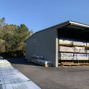 n exterior shot of a warehouse with stacks of lumber and building materials visible under a roofed area. The building is labeled 