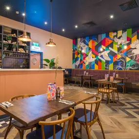 Zizzi Metro Centre, lively interior with vibrant foliage, neon lighting and bold seating.