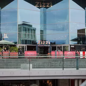 Exterior view of Zizzi Liverpool One, showing modern glass front and outdoor seating area surrounded by planted greenery.