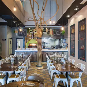 Interior view of Zizzi Liverpool One, featuring a bright, open dining space with colourful seating, mural art and tree decor.