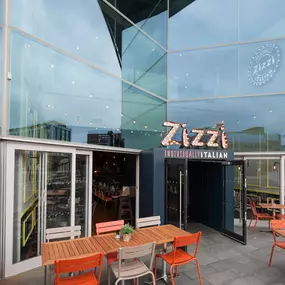 Exterior view of Zizzi Liverpool One, showing modern glass front and outdoor seating area surrounded by planted greenery.