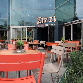 Exterior view of Zizzi Liverpool One, showing modern glass front and outdoor seating area surrounded by planted greenery.