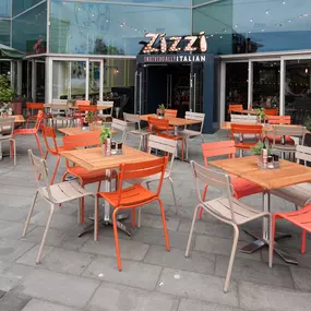 Exterior view of Zizzi Liverpool One, showing modern glass front and outdoor seating area surrounded by planted greenery.