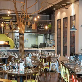 Interior view of Zizzi Liverpool One, featuring a bright, open dining space with colourful seating, mural art and tree decor.