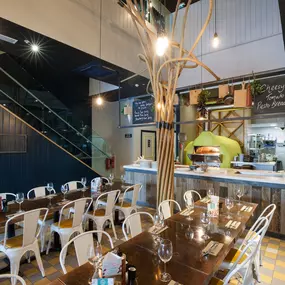 Interior view of Zizzi Liverpool One, featuring a bright, open dining space with colourful seating, mural art and tree decor.