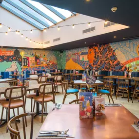 Zizzi Farnham, cozy interior with vibrant murals and hanging orange foliage.