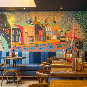 Zizzi Farnham, cozy interior with vibrant murals and hanging orange foliage.