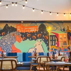 Zizzi Farnham, cozy interior with vibrant murals and hanging orange foliage.