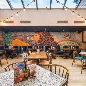 Zizzi Farnham, cozy interior with vibrant murals and hanging orange foliage.