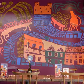 Zizzi Farnham, cozy interior with vibrant murals and hanging orange foliage.