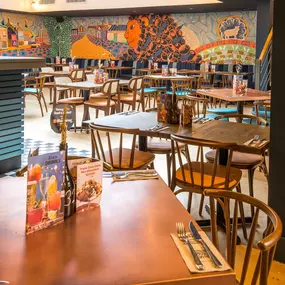 Zizzi Farnham, cozy interior with vibrant murals and hanging orange foliage.