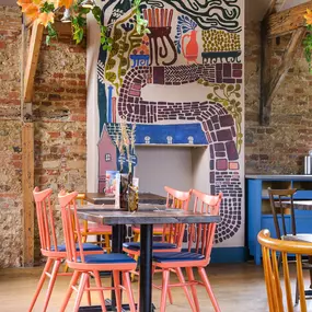 Zizzi Farnham, cozy interior with vibrant murals and hanging orange foliage.