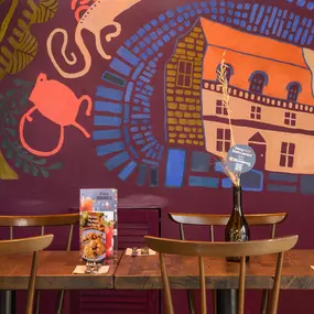Zizzi Farnham, cozy interior with vibrant murals and hanging orange foliage.