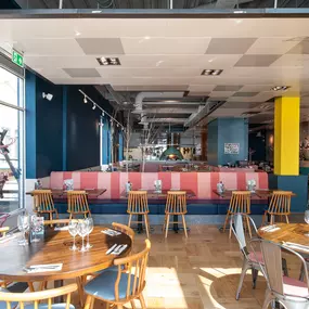 Cardiff Mermaid Quay, waterfront tables with panoramic bay views and lively mural with booth seating and pastel accents.