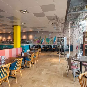 Cardiff Mermaid Quay, waterfront tables with panoramic bay views and lively mural with booth seating and pastel accents.