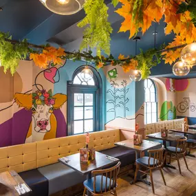 Zizzi Hereford, vibrant dining with hanging ceiling foliage and warm lighting.