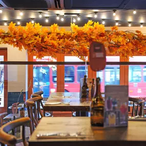 Zizzi Chiswick, showcases wooden tables and chairs beneath decorative copper foliage suspended from the ceiling.