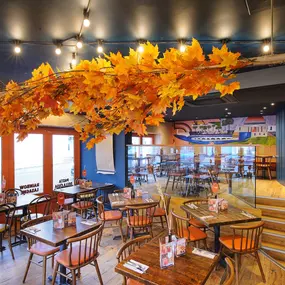 Zizzi Chiswick, showcases wooden tables and chairs beneath decorative copper foliage suspended from the ceiling.