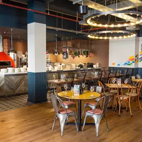 Zizzi Coventry, vibrant dining space with high ceilings and natural light, hanging decor and artistic wall art.