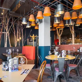 Zizzi Coventry, vibrant dining space with high ceilings and natural light, hanging decor and artistic wall art.