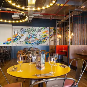 Zizzi Coventry, vibrant dining space with high ceilings and natural light, hanging decor and artistic wall art.