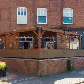 Exterior view of Zizzi St Albans terrace dining under wooden canopy and fairy lighting.