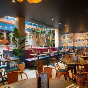 Interior view of Zizzi Maidstone, featuring vibrant wall murals, hanging foliage and bold mixed seating styles.