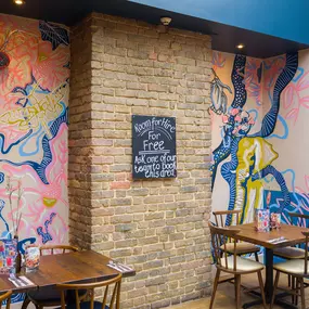 Interior view of Zizzi Maidstone, featuring vibrant wall murals, hanging foliage and bold mixed seating styles.