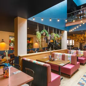 Interior view of Zizzi Maidstone, featuring vibrant wall murals, hanging foliage and bold mixed seating styles.