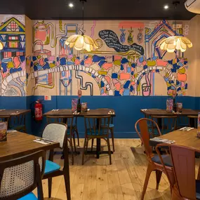 Interior view of Zizzi Maidstone, featuring vibrant wall murals, hanging foliage and bold mixed seating styles.