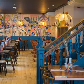 Interior view of Zizzi Maidstone, featuring vibrant wall murals, hanging foliage and bold mixed seating styles.
