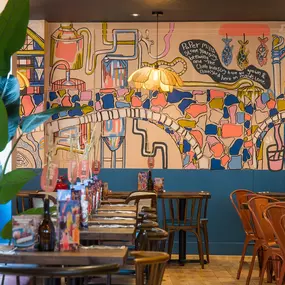 Interior view of Zizzi Maidstone, featuring vibrant wall murals, hanging foliage and bold mixed seating styles.