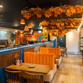 Zizzi - Glasgow Princes Square, vibrant interior with banquet seating and gallery views, and orange foliage creating an inviting atmosphere.