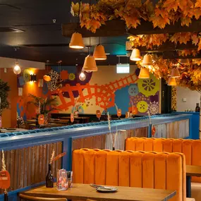 Zizzi - Glasgow Princes Square, vibrant interior with banquet seating and gallery views, and orange foliage creating an inviting atmosphere.