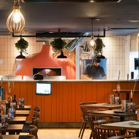 Zizzi - Glasgow Princes Square, vibrant interior with banquet seating and gallery views, and orange foliage creating an inviting atmosphere.